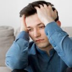 man looking downward holding forehead