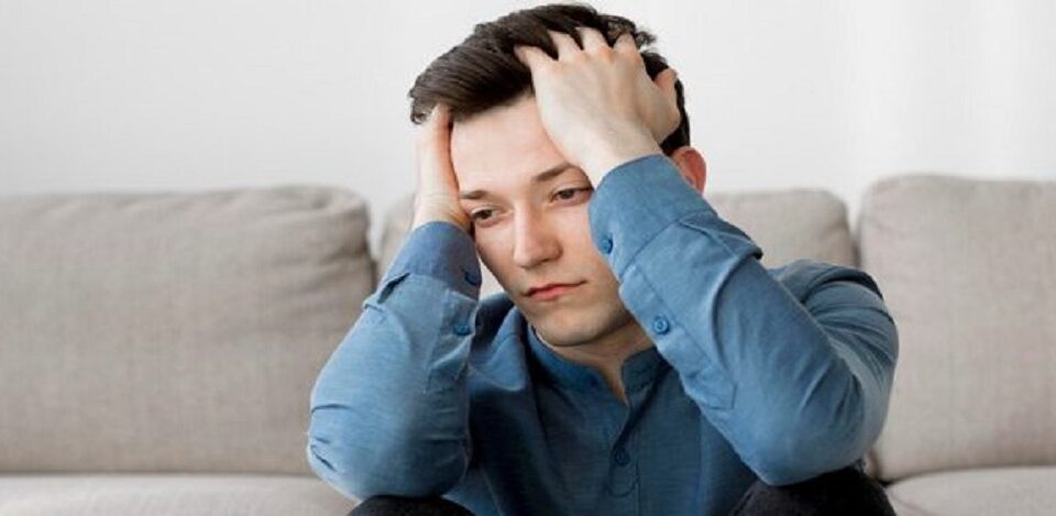 man looking downward holding forehead