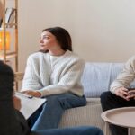 Couple sitting in front of counselor facing opposite to each other.